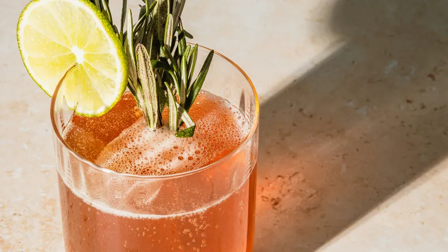 Pink cocktail with lime and rosemary garnish.