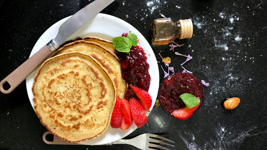 Pancakes with strawberries and jam on plate.