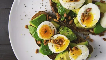 Avocado-Toast mit Eiern und Pinienkernen auf Teller.