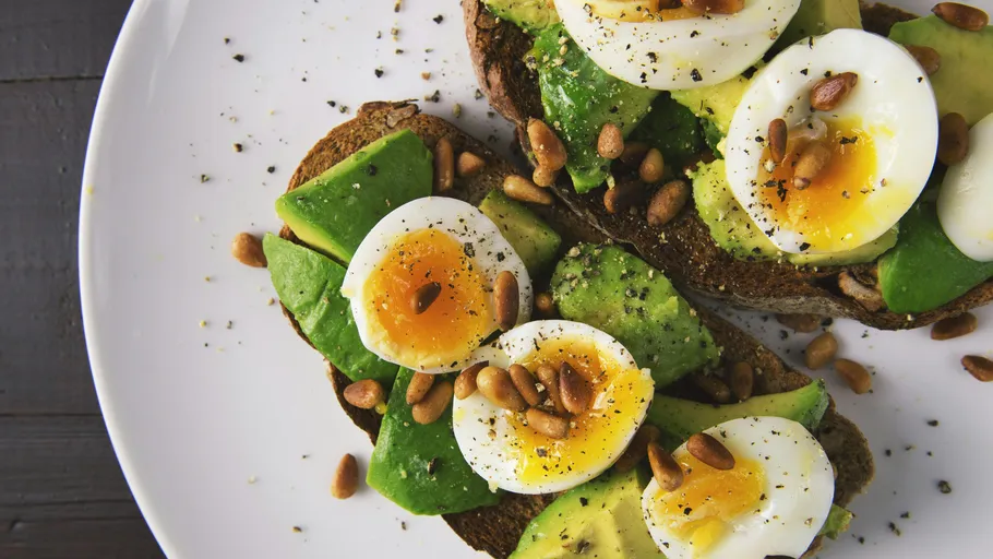 Avocado toast with eggs and pine nuts on plate.