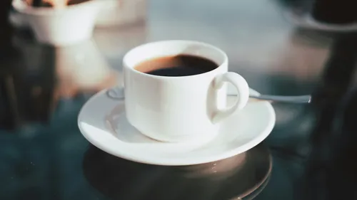 Coffee cup on saucer, reflective table surface.