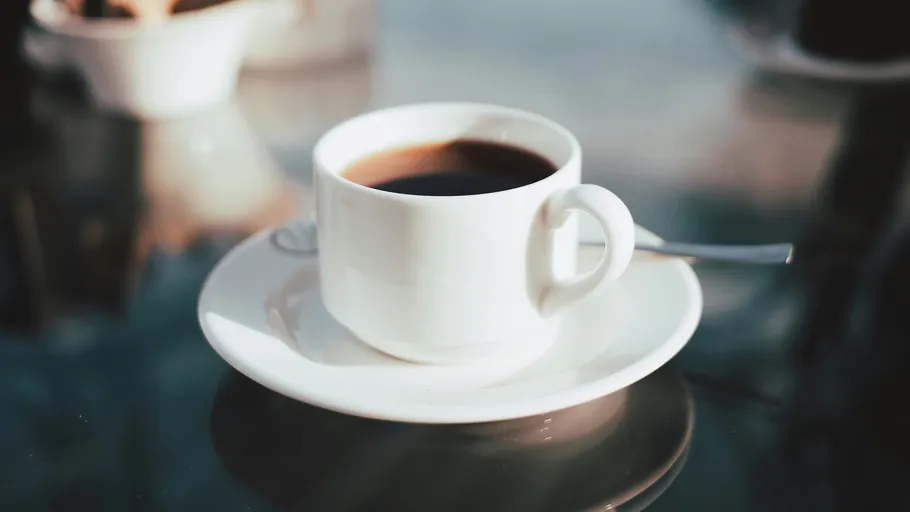 Kaffeetasse auf Untertasse, reflektierende Tischoberfläche.