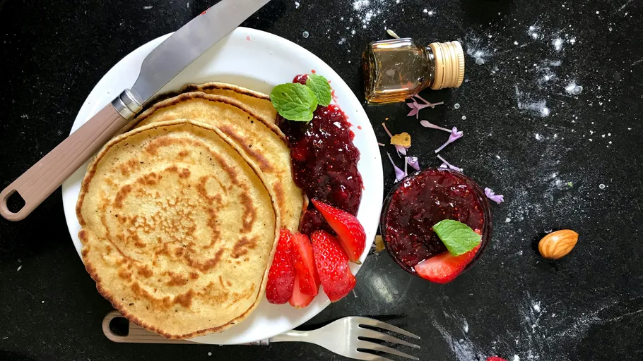 Pancakes with strawberries and jam on plate.
