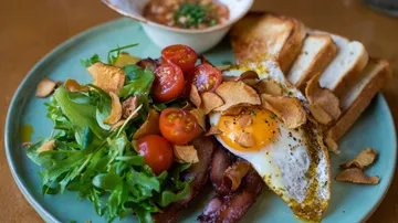 Breakfast plate with bacon, eggs, salad, toast, sauce.