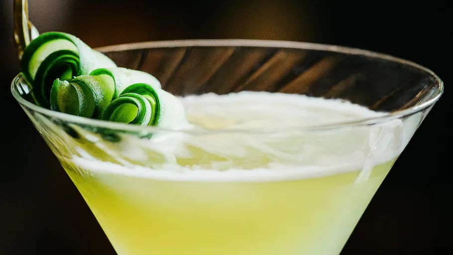 Grüner Cocktail mit Gurkendekoration im Glas.