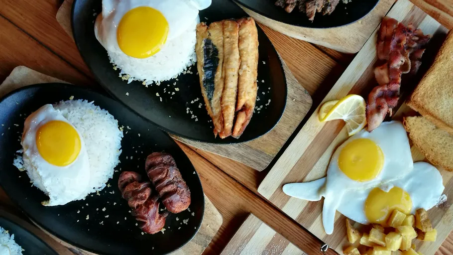 Plates of rice, eggs, fish, sausage, and toast.