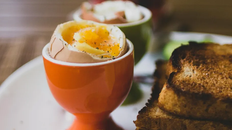 Weichgekochtes Ei im Becher mit Toast daneben.