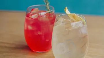 Two cocktails with ice on a wooden table.