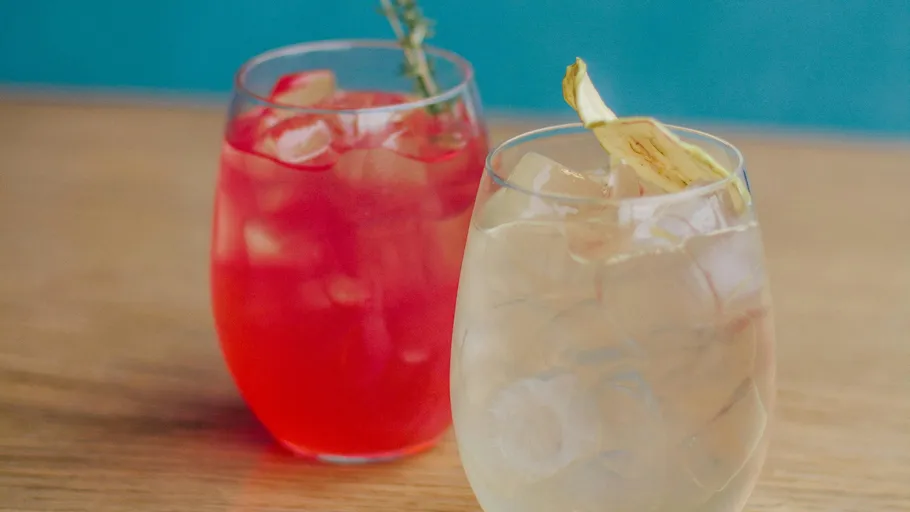 Two cocktails with ice on a wooden table.