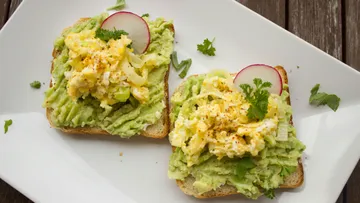 Avocado toast with scrambled eggs and garnish.