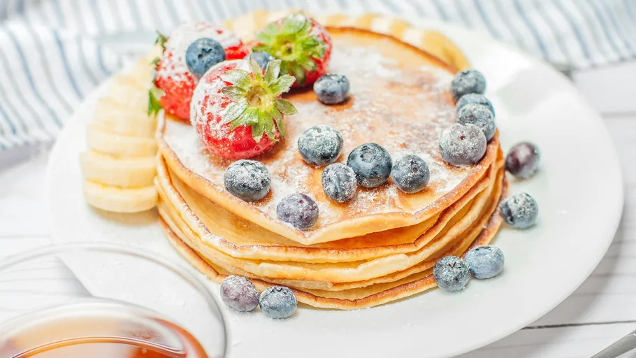 Stacked pancakes topped with berries on plate.