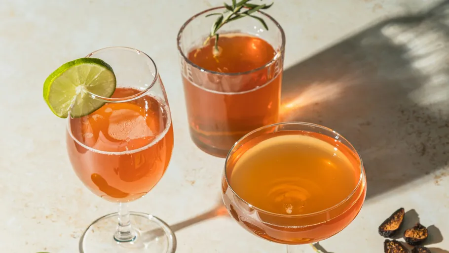 Drei Cocktails mit Limette und Kräutern auf Tisch.