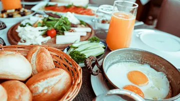Frühstück mit Eiern, Brötchen und Saft auf Tisch.