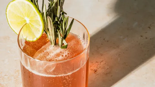 Glass with red drink, lime, and rosemary.