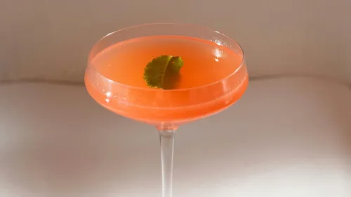 Pinkfarbener Cocktail im Glas mit Blattgarnitur.