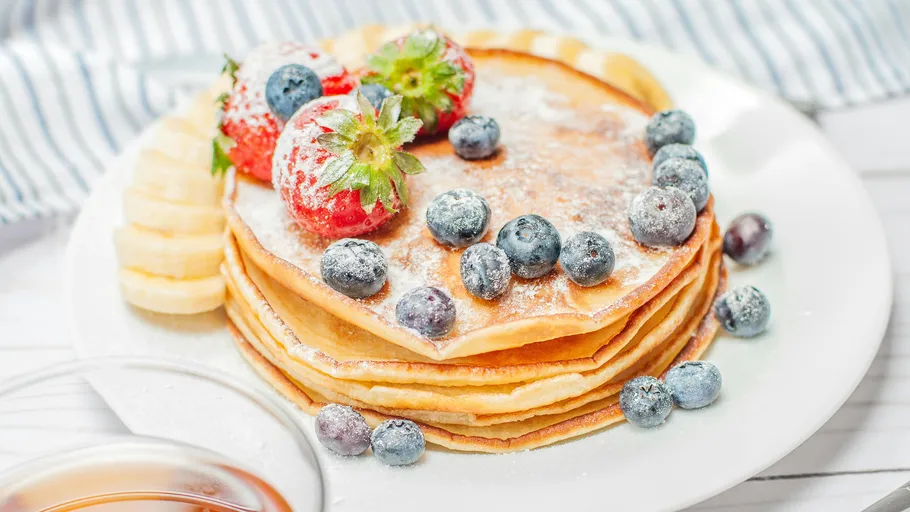 Stacked pancakes with fruit toppings on plate.
