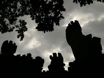 Ruine umgeben von Bäumen, gegen einen bewölkten Himmel.
