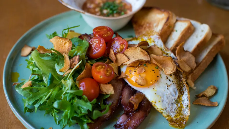Teller mit Frühstück: Eier, Speck, Salat.