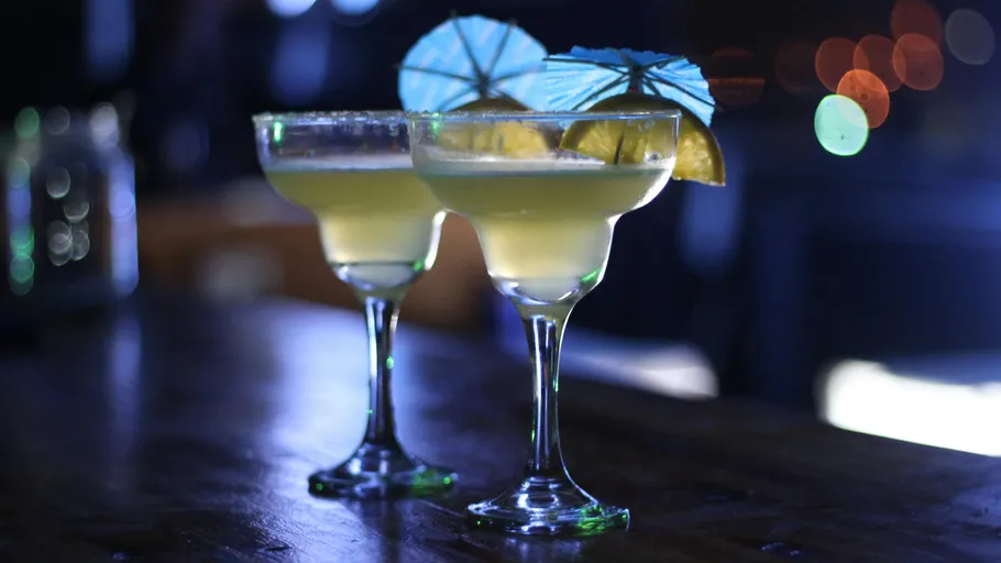 Zwei Cocktails auf Holztisch, schwach beleuchtet.