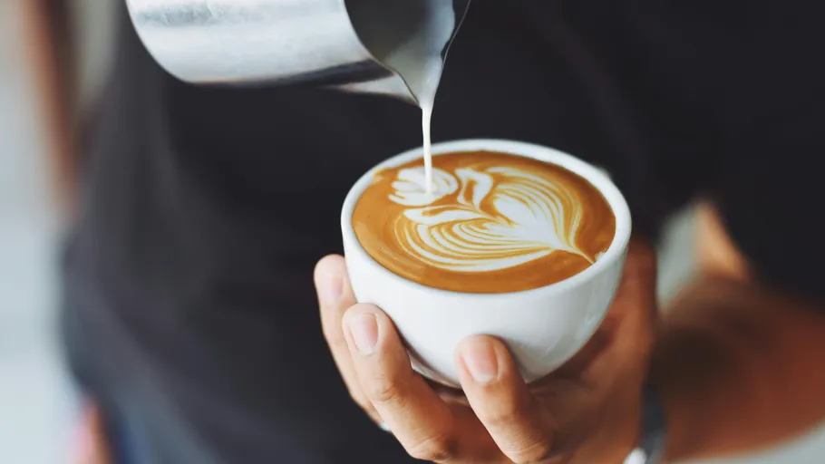 Person pouring latte art in coffee cup.