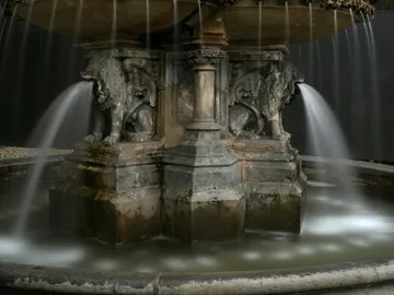 Brunnen mit Wasserstrahlen fließt um Löwenfiguren, dunkel.