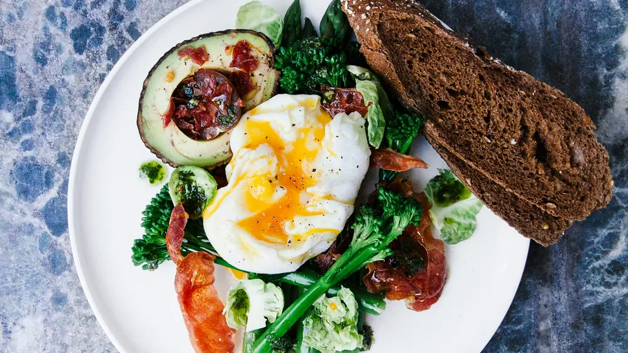 Pochiertes Ei mit Avocado, Gemüse und Brot.