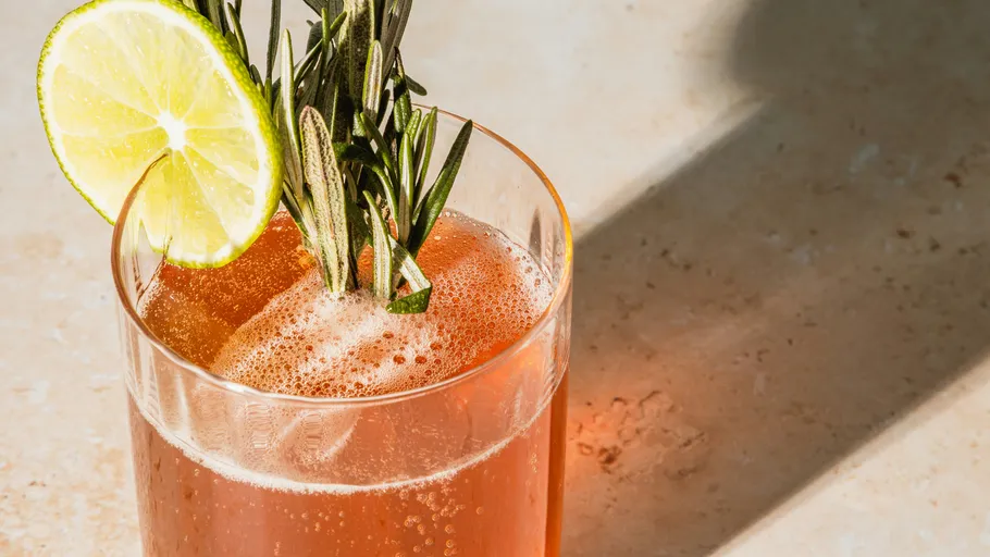 Red drink with lime and rosemary garnish.