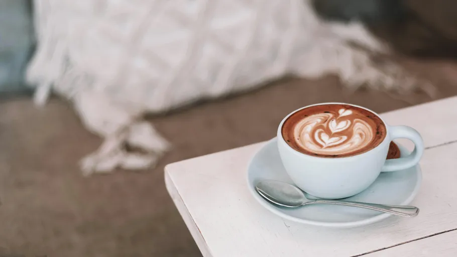 Tasse Cappuccino auf weißem Tisch, gemütliche Umgebung.