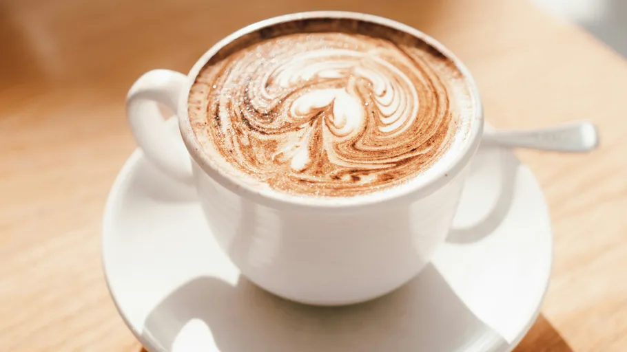 Kaffeetasse mit Latte Art auf Tisch.