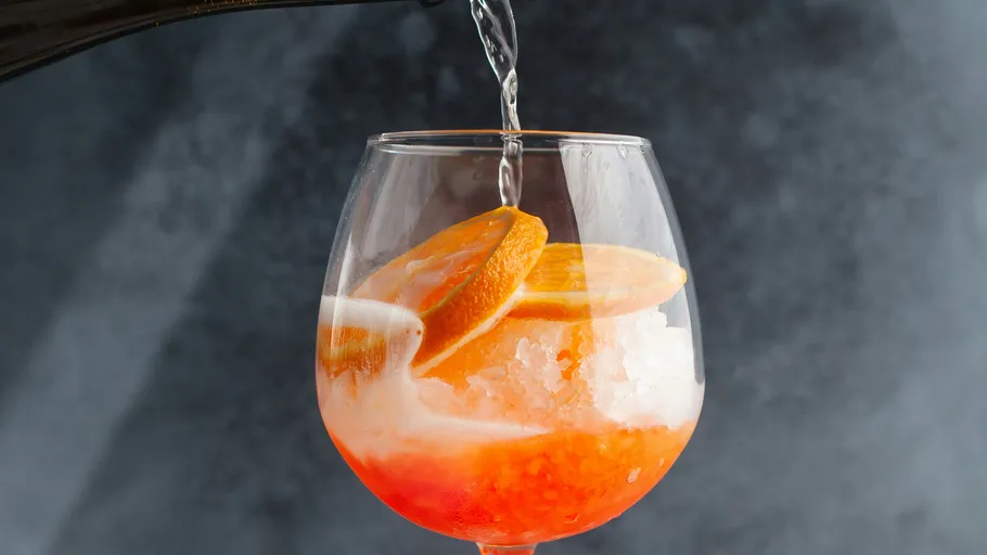 Glas mit Orangenscheiben, Getränk wird eingeschenkt.