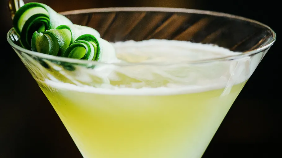 Green cocktail with cucumber garnish in glass.