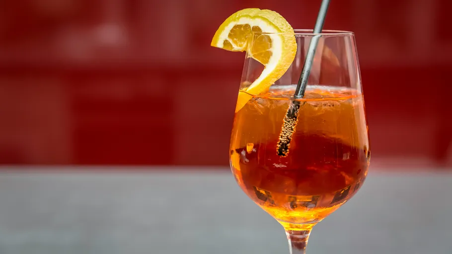 Orangener Cocktail mit Zitronenscheibe und Strohhalm.