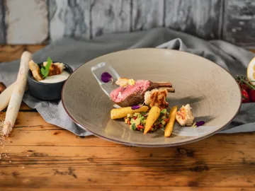 A rounded plate with lamb, vegetables, and sauces.