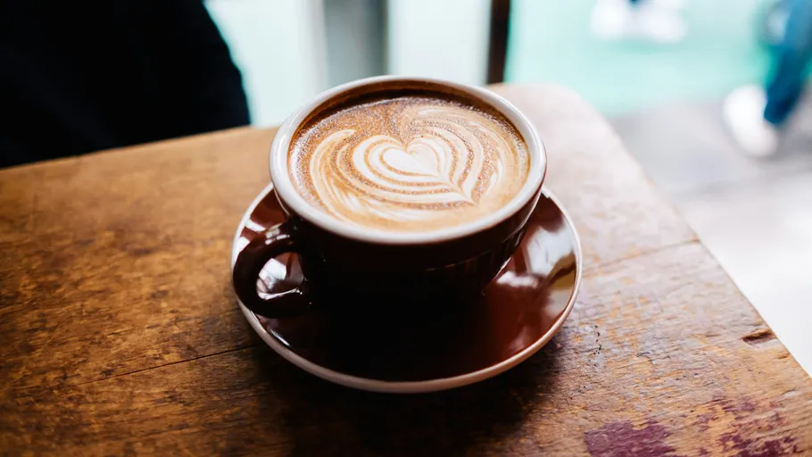 Kaffeetasse mit Herz-Latte-Art auf Tisch.