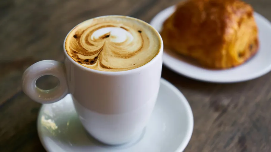 Kaffeetasse mit Latte-Art, Gebäck in der Nähe.