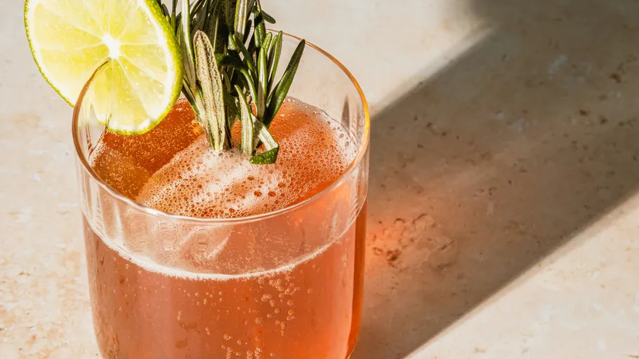 Rosa Getränk mit Limette und Rosmarin auf Tisch.
