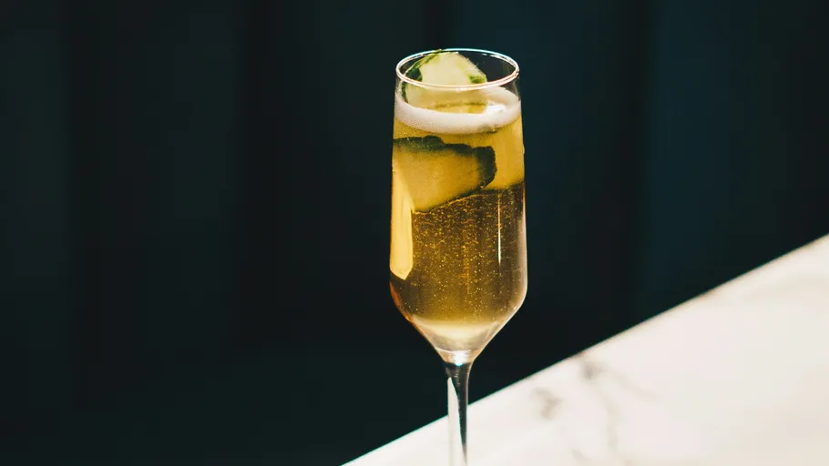 Hohe Champagnerglas mit Gurkenscheiben auf Tisch.