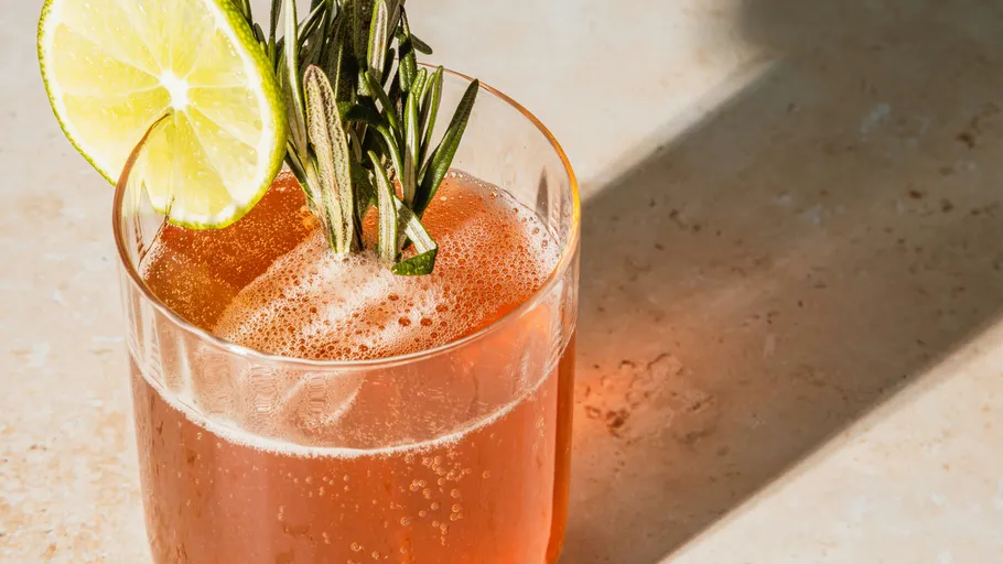 Glass with orange drink, lime, rosemary garnish.