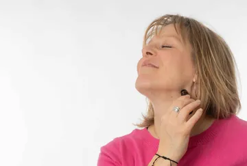 Person applying perfume on neck, smiling.