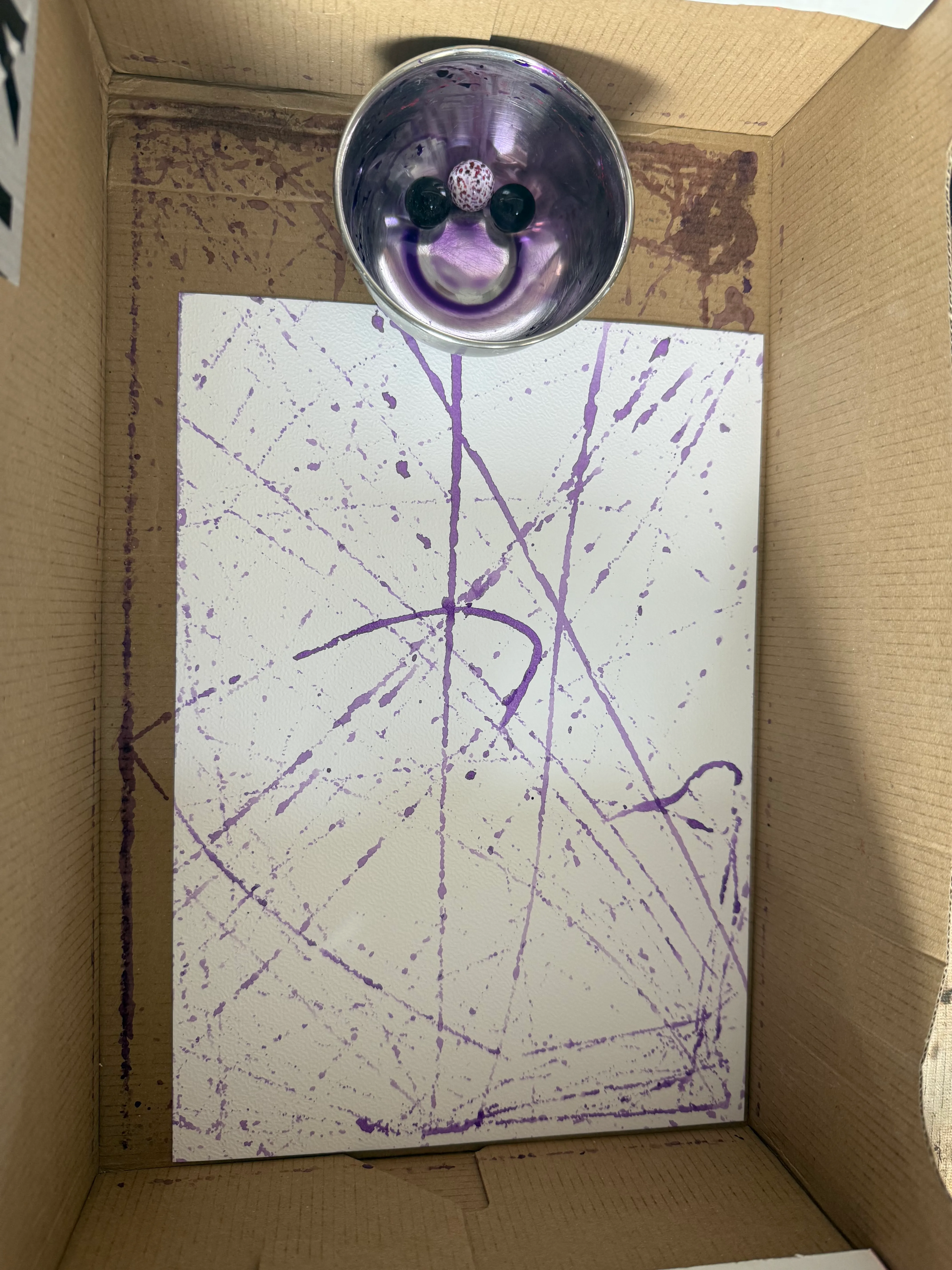 Papier in einem Karton mit lila Farbspritzern.