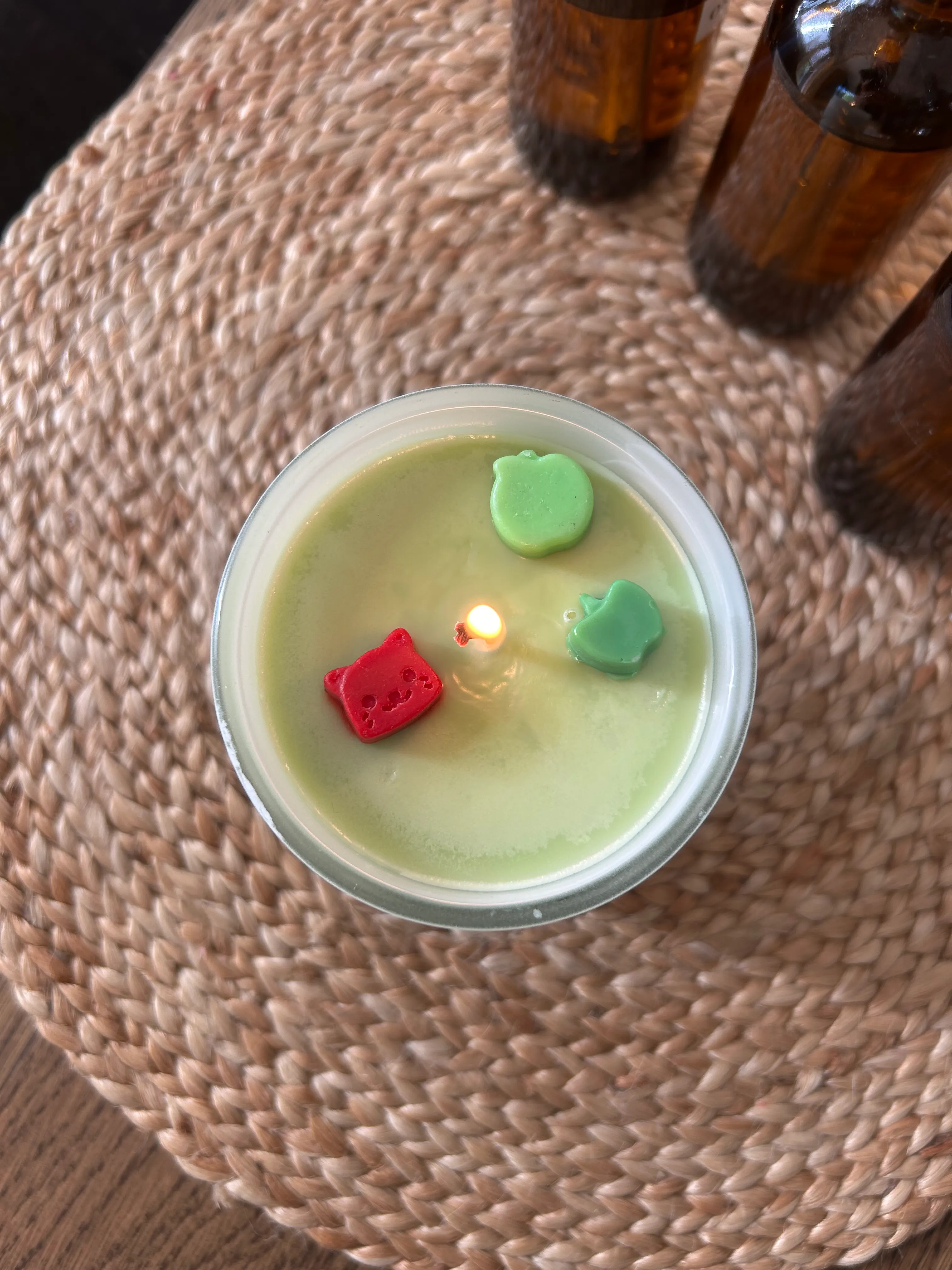 Kerze mit bunten Wachselementen, auf geflochtenem Untersetzer.