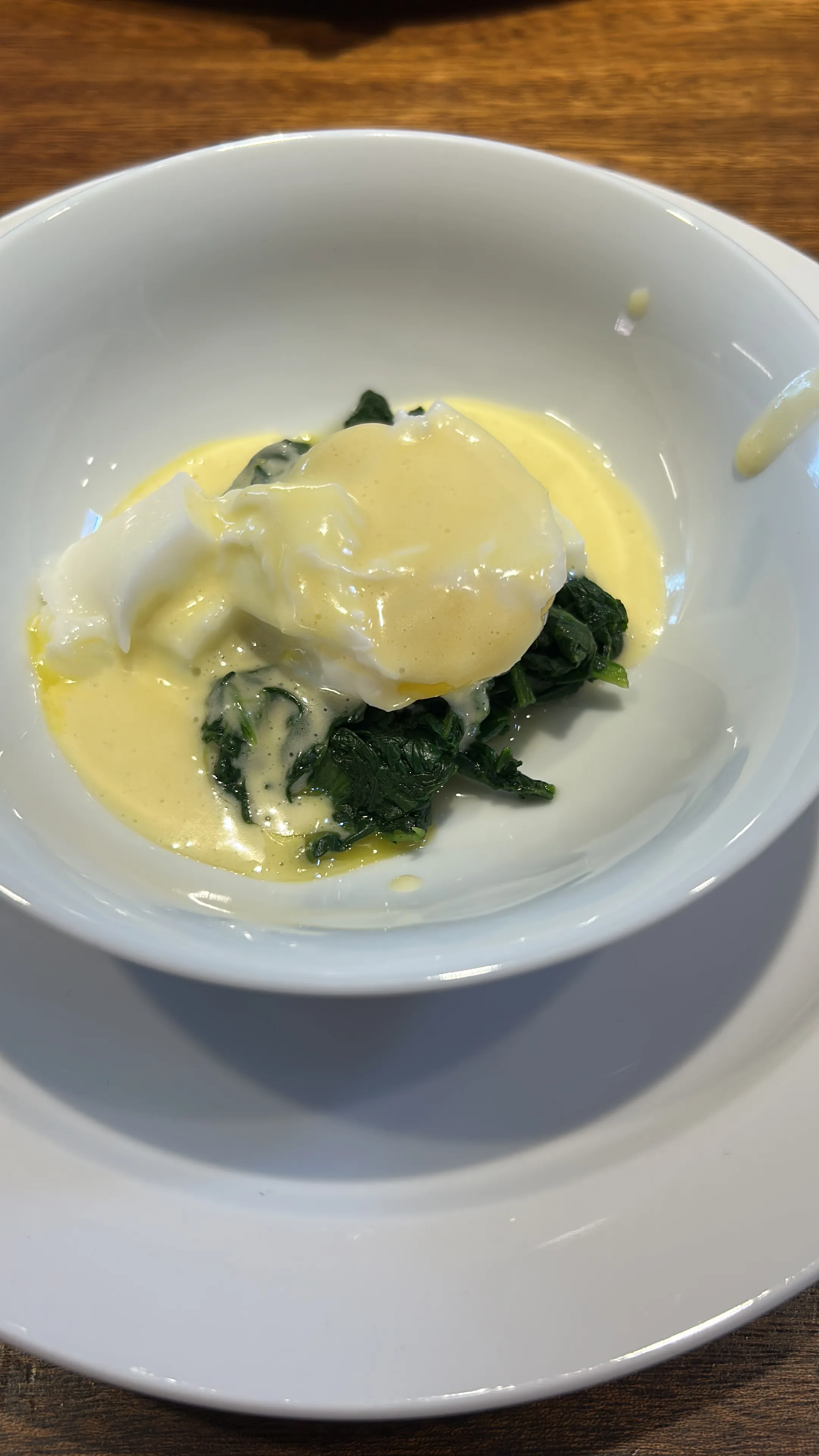 Pochiertes Ei mit Sauce auf Spinat, weiße Schüssel.