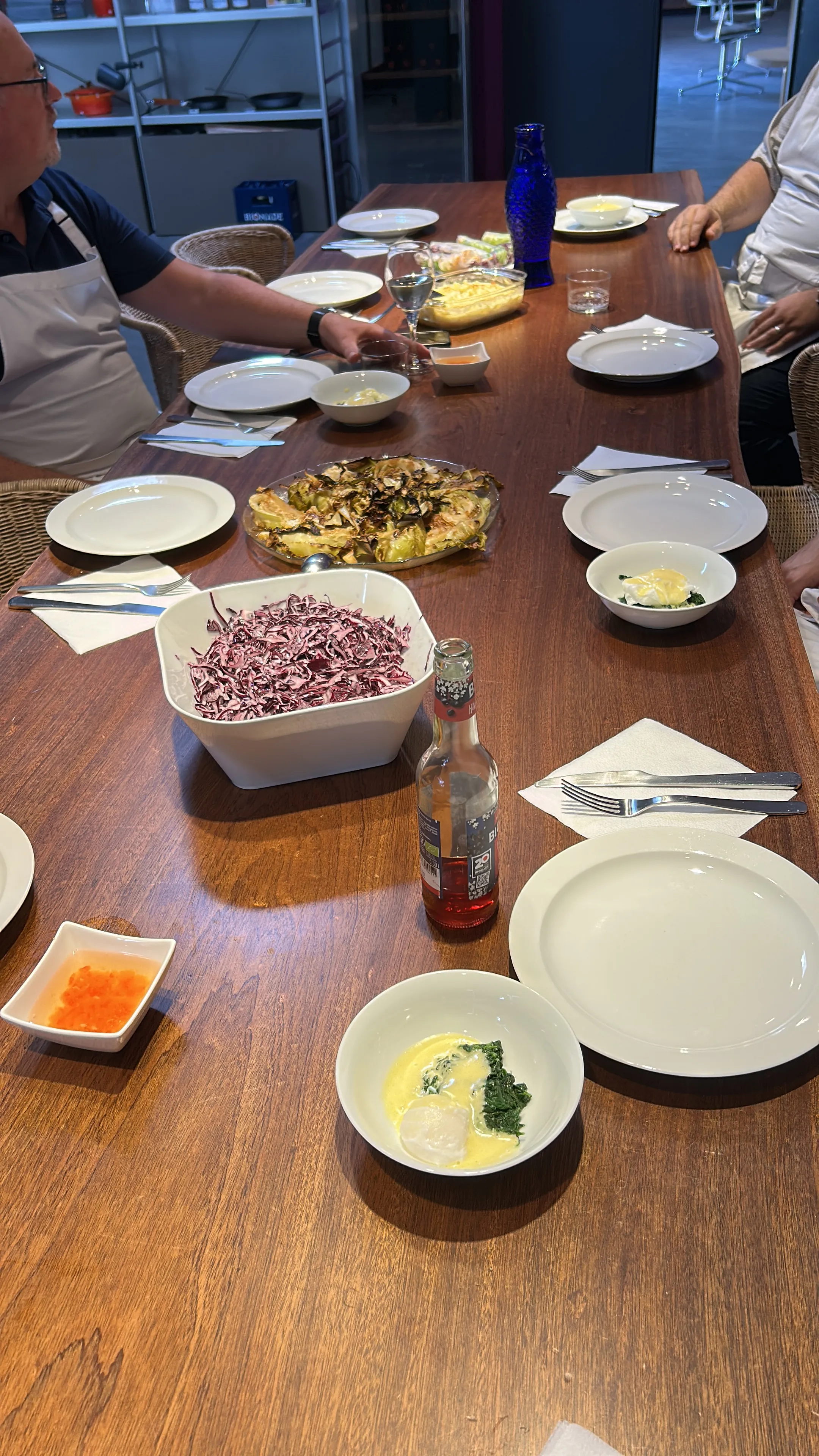 Esstisch mit Essen und sitzenden Personen.