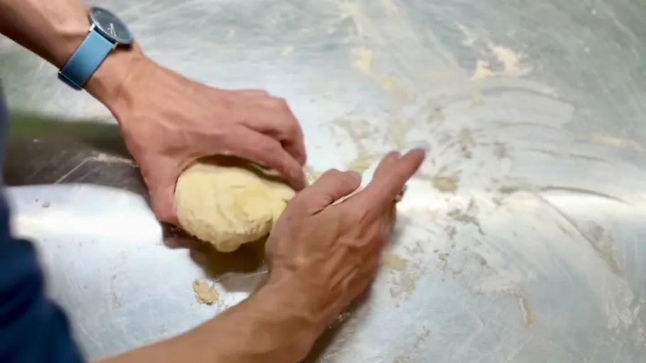 Hands kneading dough on metallic surface.