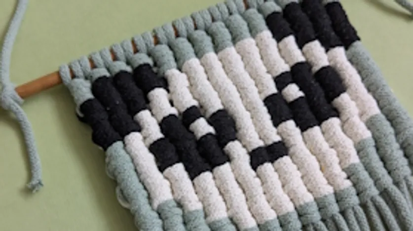 Woven wall hanging with abstract pattern, pastel colors.