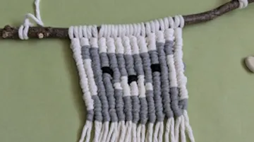 Macrame tapestry with cat design on stick.