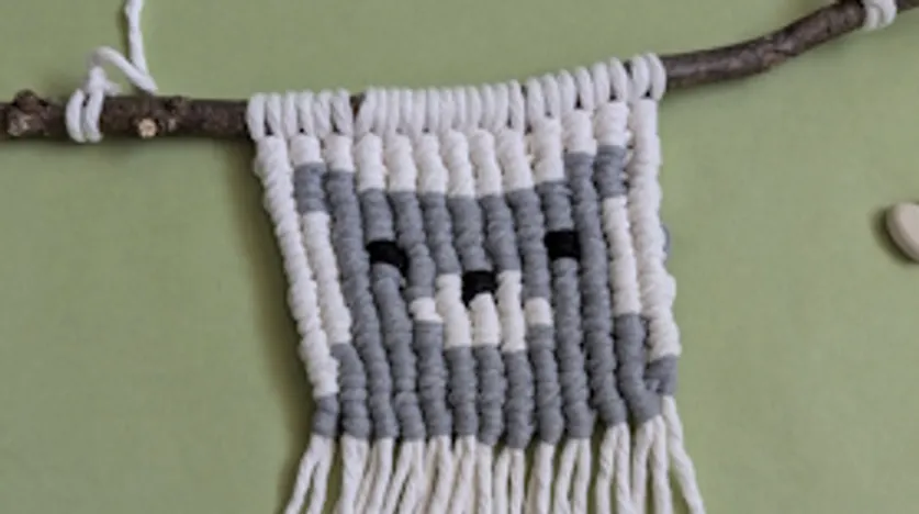 Makramee-Wandbehang mit Katzendesign auf Ast.