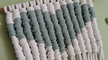 Macrame wall hanging with green and white pattern.