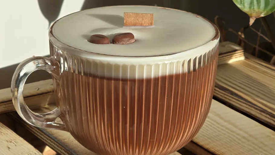 Glasbecher mit cremigem Kaffee auf Holztisch.