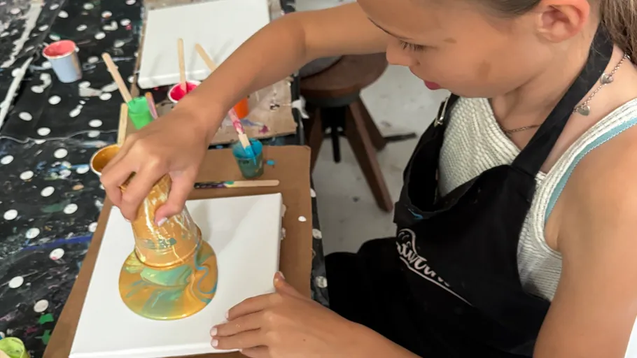 Child pouring paint on canvas in studio.
